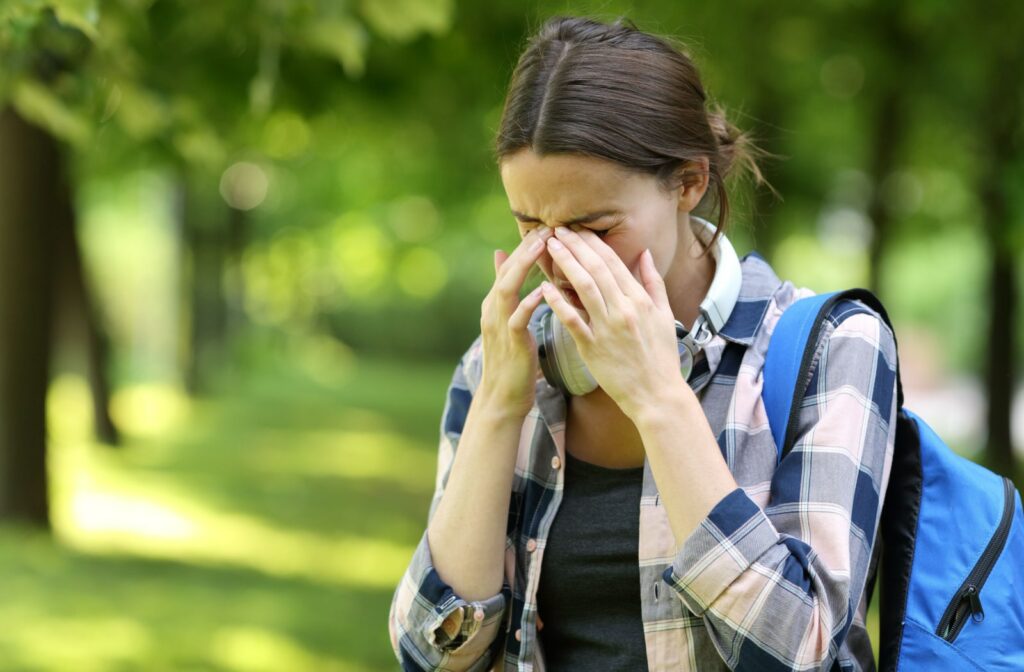 A female student in a park experiencing dry eyes, scratching her itchy eyes