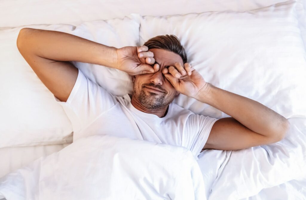 A man lying in bed rubbing his eyes with his hands.