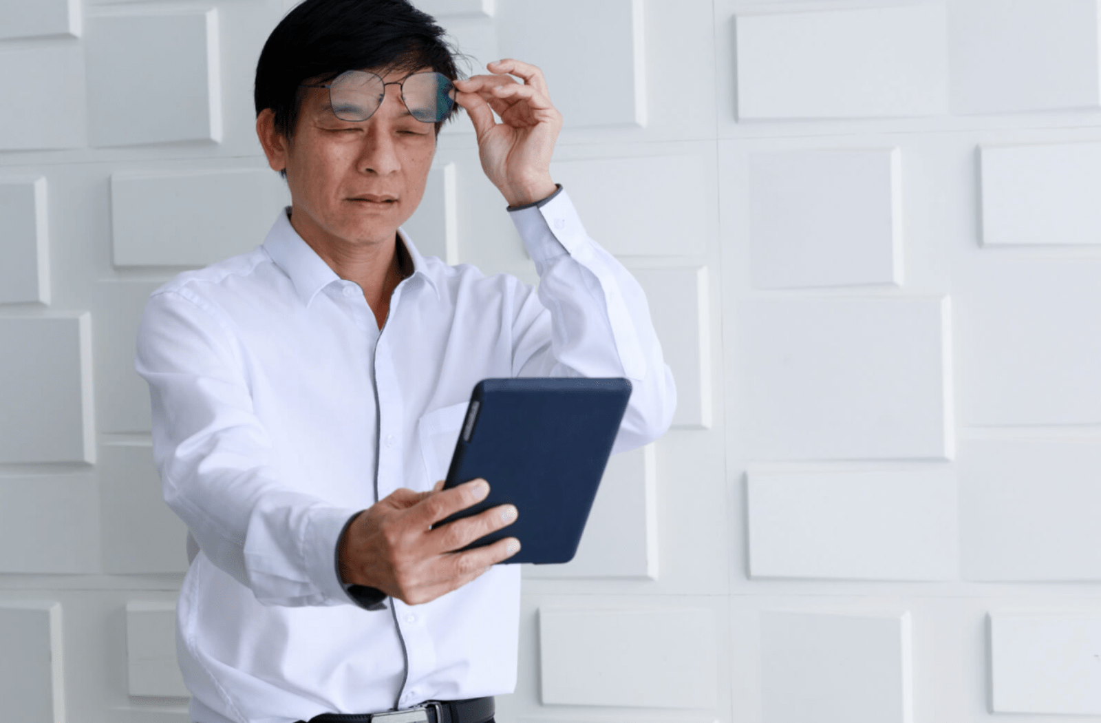 A mature man is holding his tablet away from his face while looking at the screen.