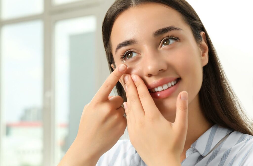 A young woman smiling while using her right hand to put in a specialty contact lens.