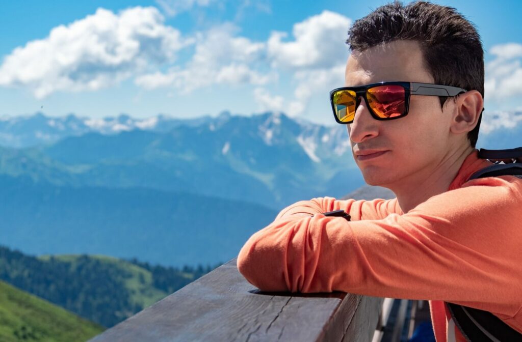A young man wearing polarized sunglasses admiring a view of the mountains on a sunny day.