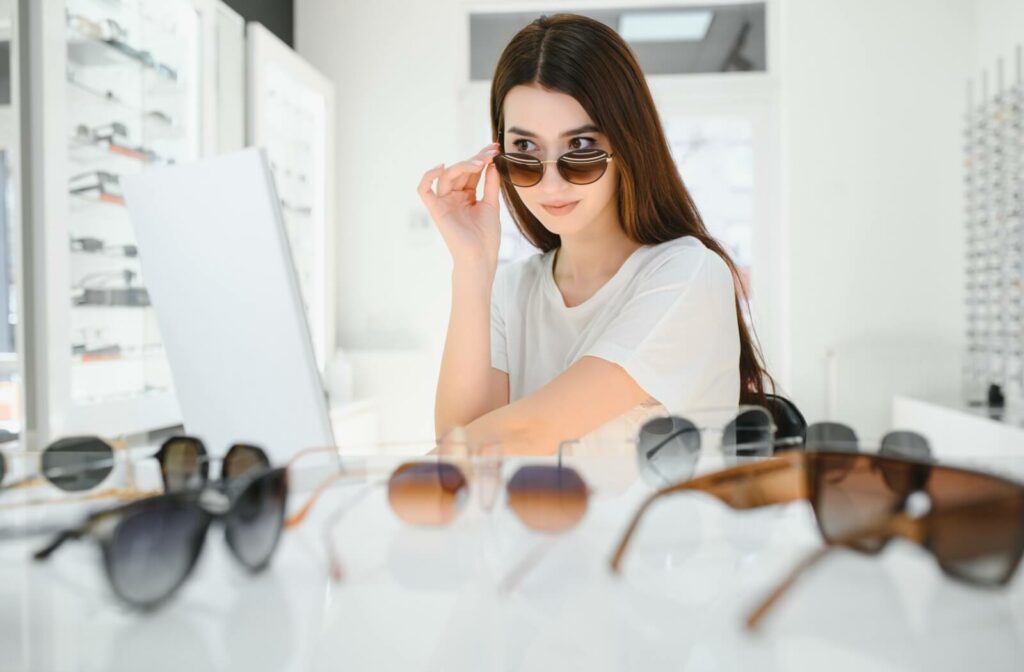 A young person with long brown hair trying on a selection of sunglasses.