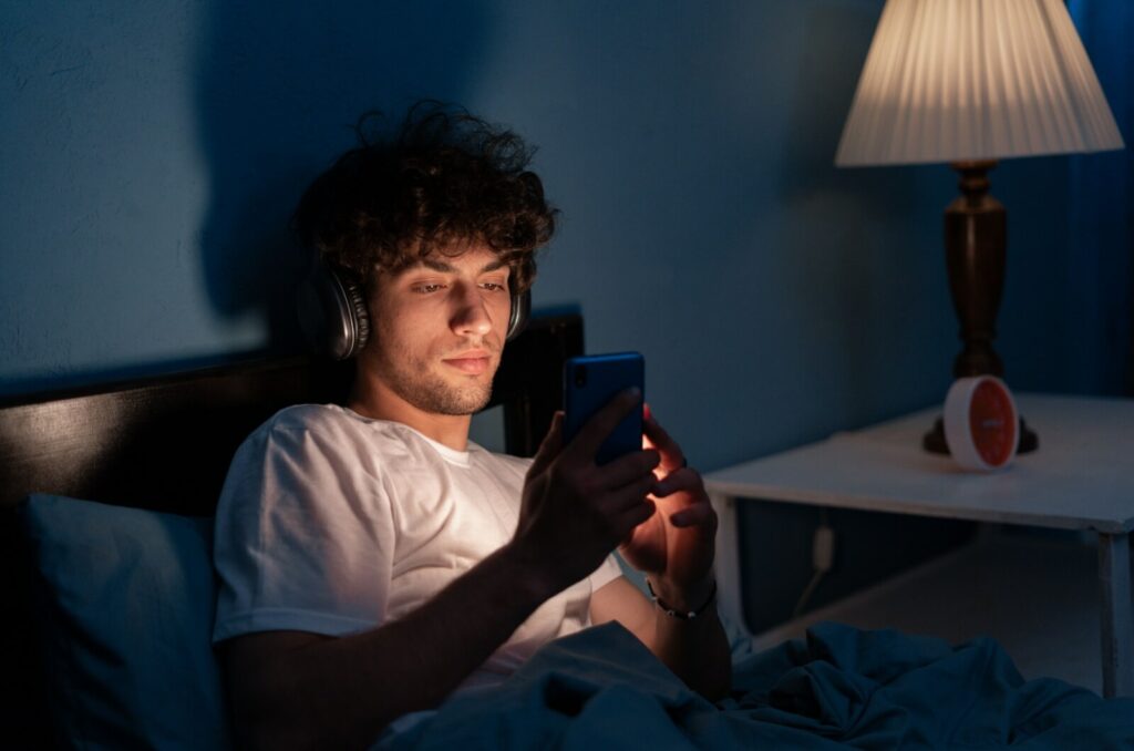 A young adult uses their phone without dark mode turned on, increasing the chances the device use can affect their eyes and sleep.