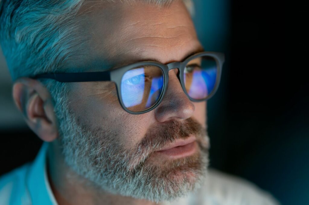 An older adult wears blue-light filtering glasses while using their computer in low-light conditions.