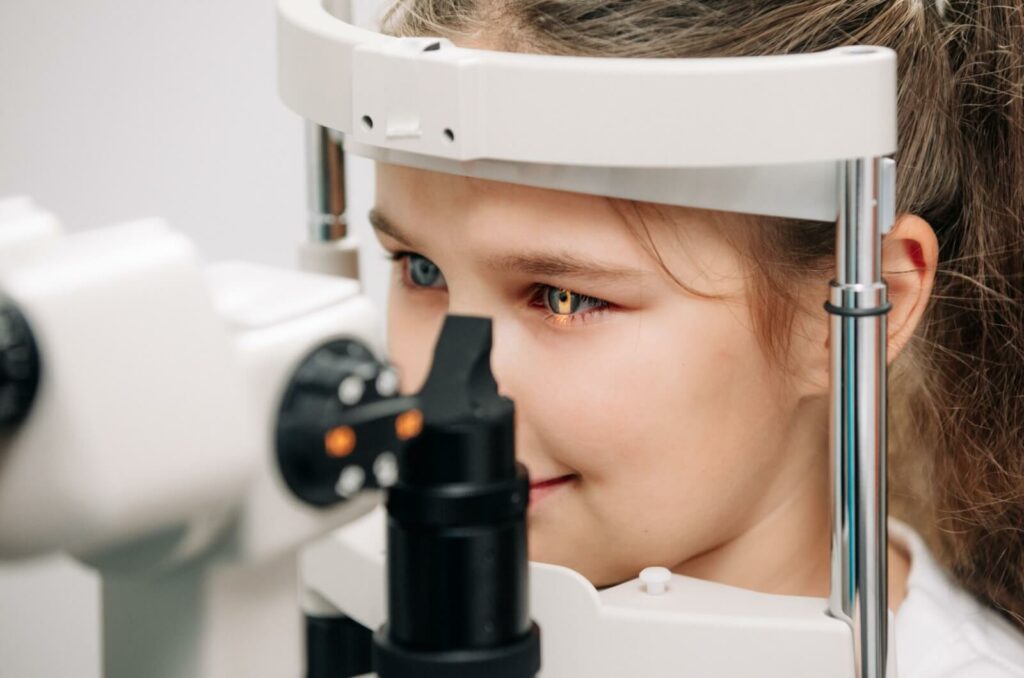 A young child smiles as they look into a machine as part of a comprehensive eye exam