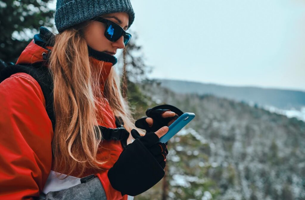 A person looks down at the map on their phone while they are out on a hike while wearing sunglasses.